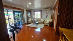 A spacious living room with a wooden floor, two beige sofas, a coffee table, and a large window with curtains. - Axis Apartments (Suva)