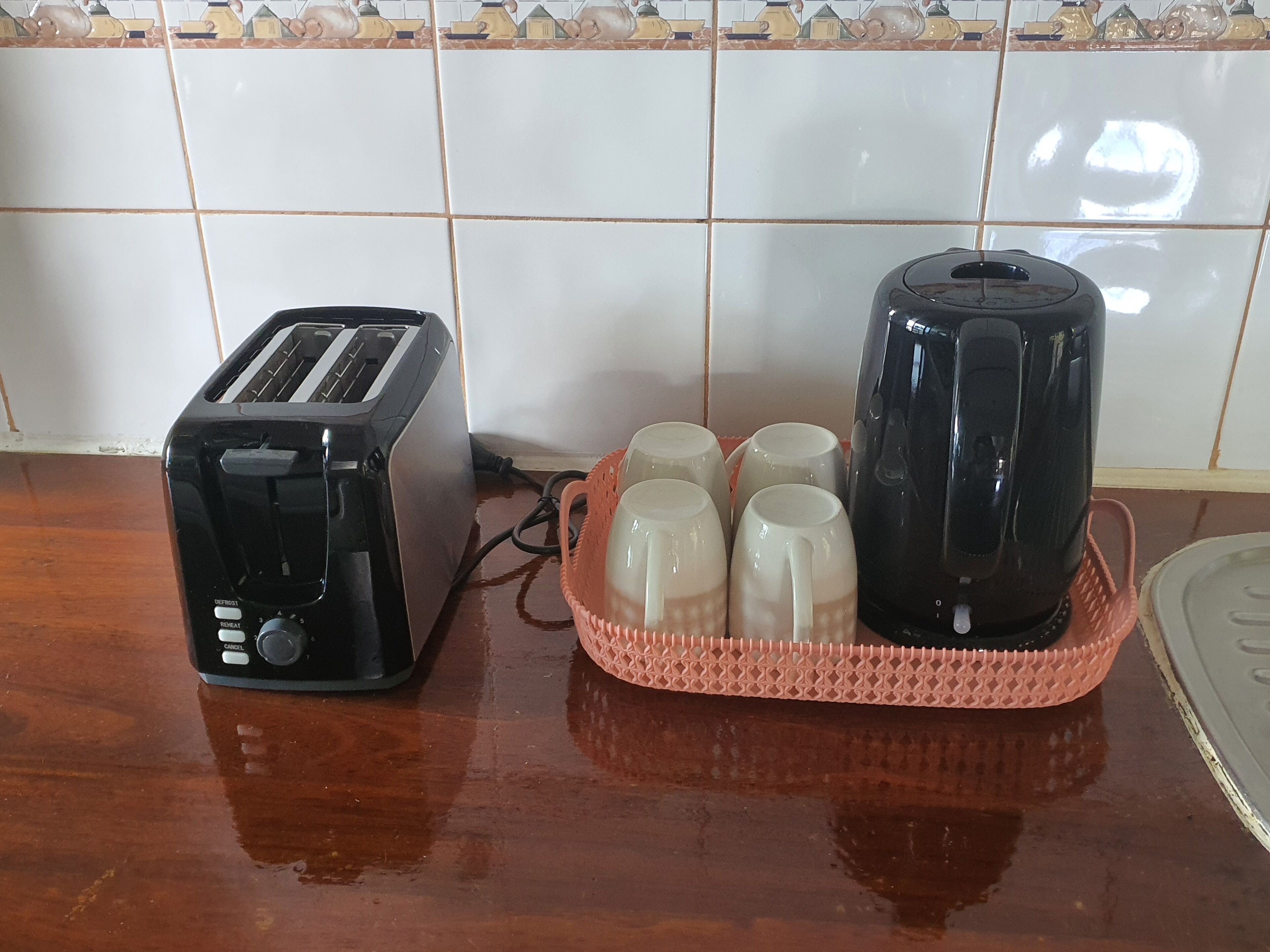 Una encimera de cocina con un tostador, una tetera y una cesta de tazas.