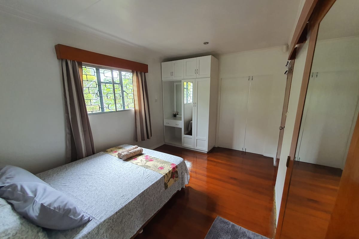 A bedroom with a bed, a wardrobe, a mirror, and a window with curtains.