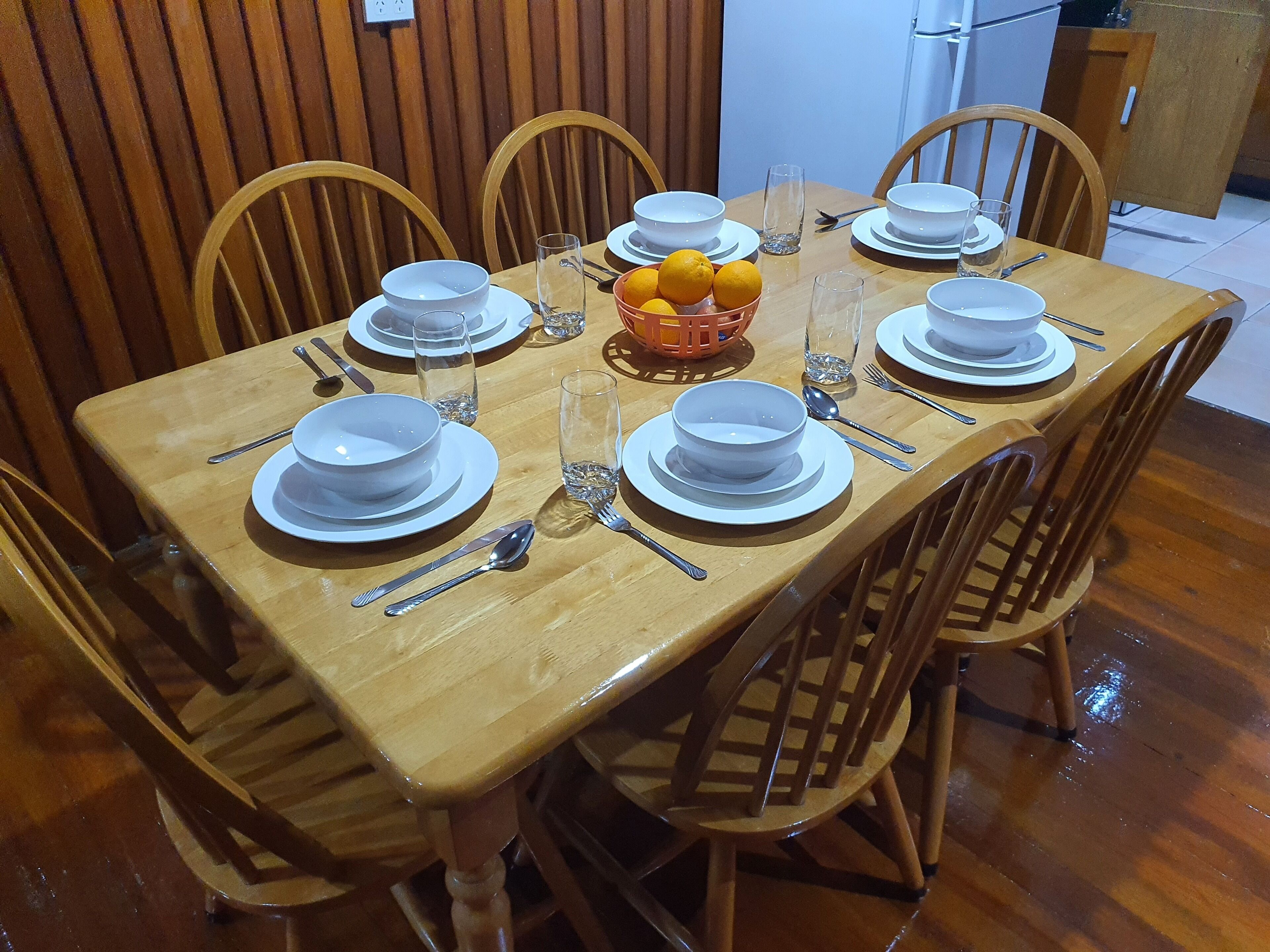 A dining table set with white plates, bowls, and cutlery, surrounded by wooden chairs.
