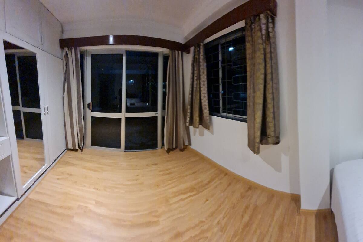 A hotel room with a bed, a nightstand, a desk, a chair, a wardrobe, and a large window with curtains.