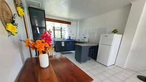 A modern kitchen with a wooden dining table, a white refrigerator, and a built-in island. - Axis Apartments (Suva)