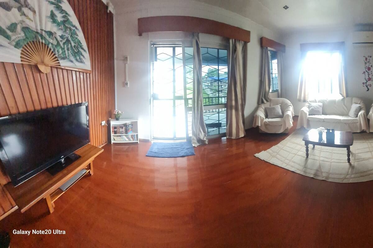 A spacious living room with a flat-screen TV, wooden flooring, and a dining area with a table and chairs.