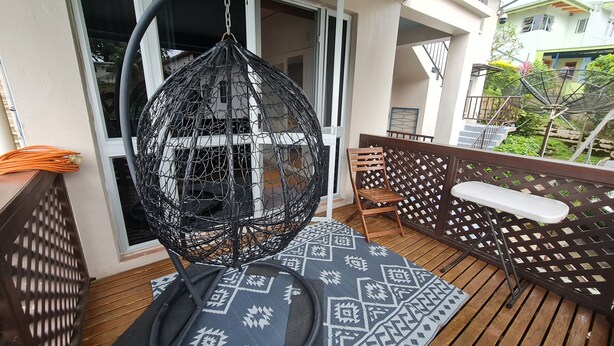 A balcony with a hanging chair, wooden furniture, and a patterned rug. - Axis Apartments (Suva)