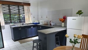 A modern kitchen with dark blue cabinets, a granite countertop, and a central island with stools. - Axis Apartments (Suva)