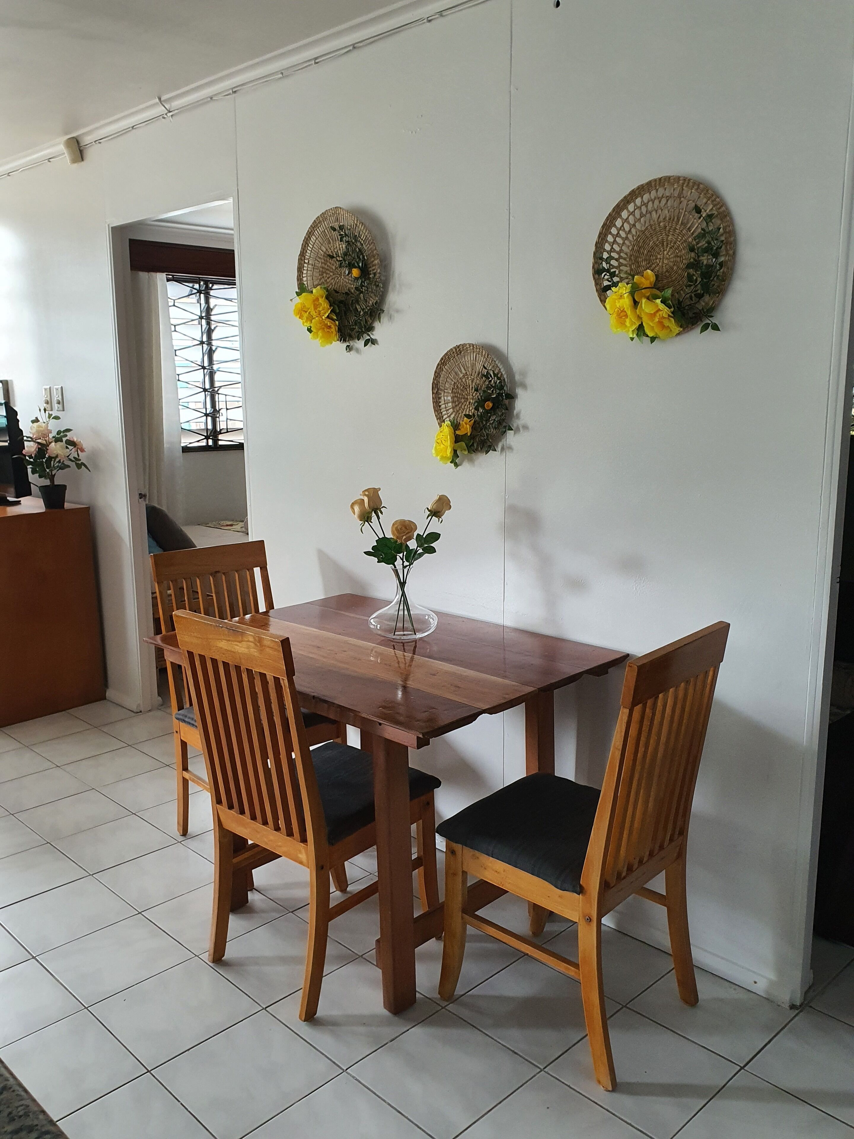A dining area with a wooden table and chairs, a vase with flowers, and decorative wall hangings.