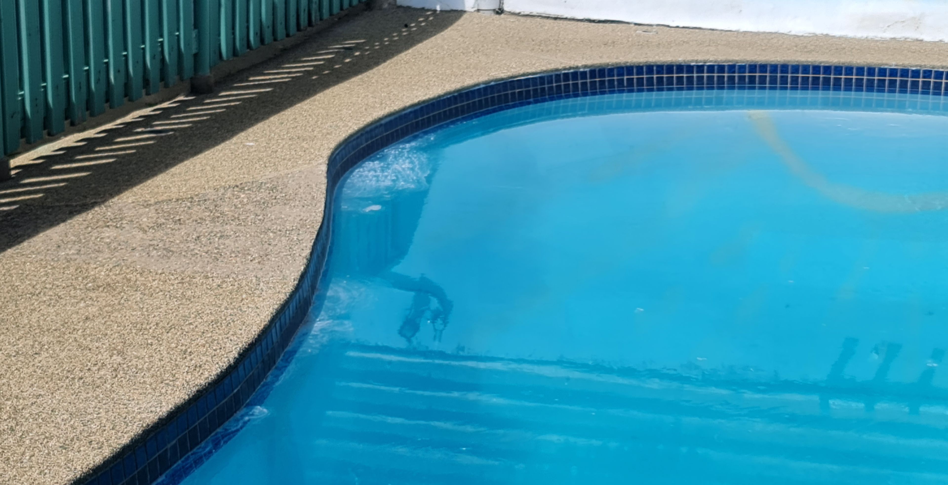 Una piscina con borde de azulejos y zona de solárium texturizado.