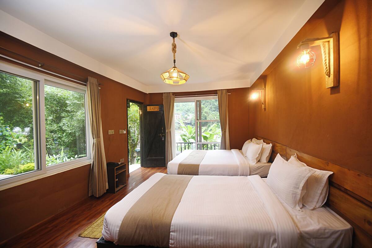 Habitación de hotel con dos camas, ventanas amplias, techo de madera y una lámpara colgante.