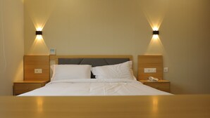 A neatly made bed with white linens, two bedside tables with lamps, and a wooden headboard. - Dreamotel Luxury Suites and Rooms (Palakkad)