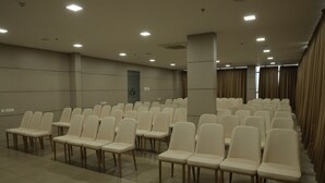 A conference room with rows of white chairs and a large pillar. - Dreamotel Luxury Suites and Rooms (Palakkad)