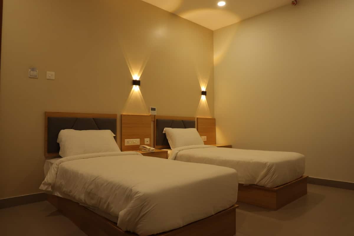 Une chambre d’hôtel avec deux lits simples, des têtes de lit en bois, des tables de chevet avec des lampes et une décoration aux couleurs neutres.