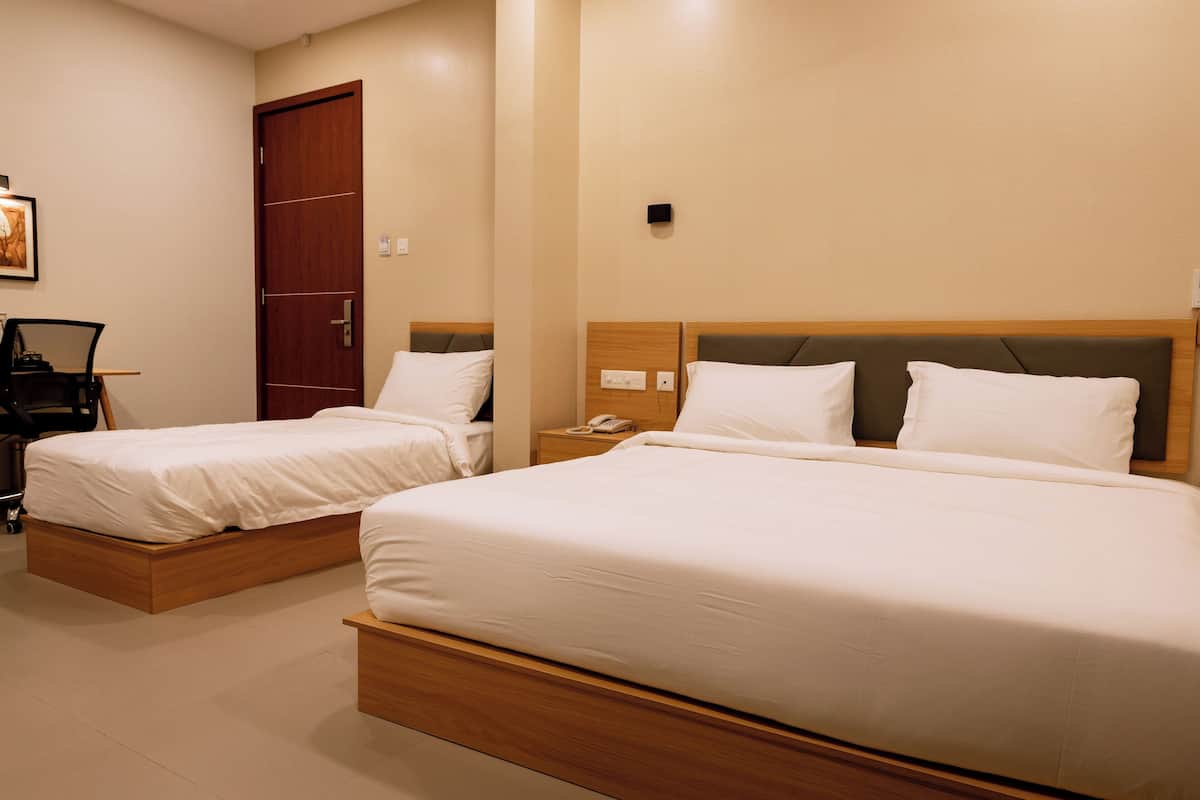 Une chambre d’hôtel avec deux lits simples, une tête de lit en bois, une table de chevet avec un téléphone et une porte.