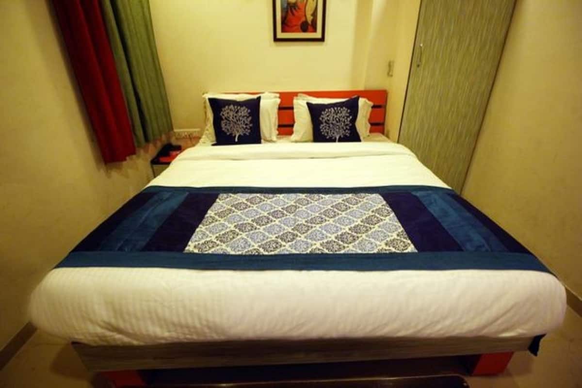 Una cama con una colcha estampada, dos almohadas con diseño de árboles y un cuadro en la pared.