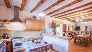 A rustic kitchen with exposed wooden beams, a gas stove, and a dining area with a table set for two. - Villa in Manacor with Pool and Tennis Court (Manacor)