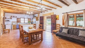A spacious living area with a wooden dining table, a sofa, and a kitchen in the background. - Villa in Manacor with Pool and Tennis Court (Manacor)