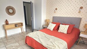 A bedroom with a bed, bedside tables, a mirror, a dresser, and a door leading to another room.