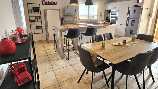 A modern kitchen with a dining area, featuring a large wooden table, black chairs, and a kitchen island with a built-in oven and microwave.