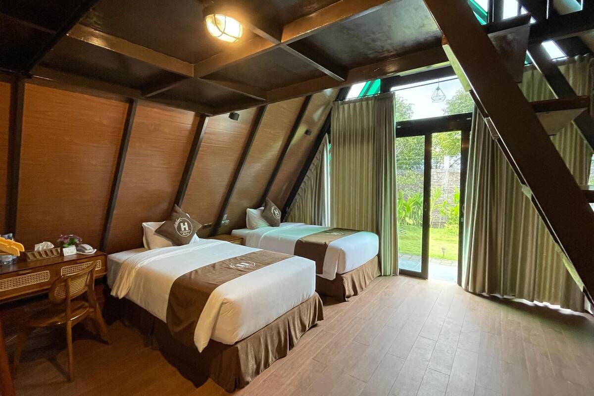 Ein Zimmer mit zwei Betten, Holzmöbeln und Blick auf Grün.