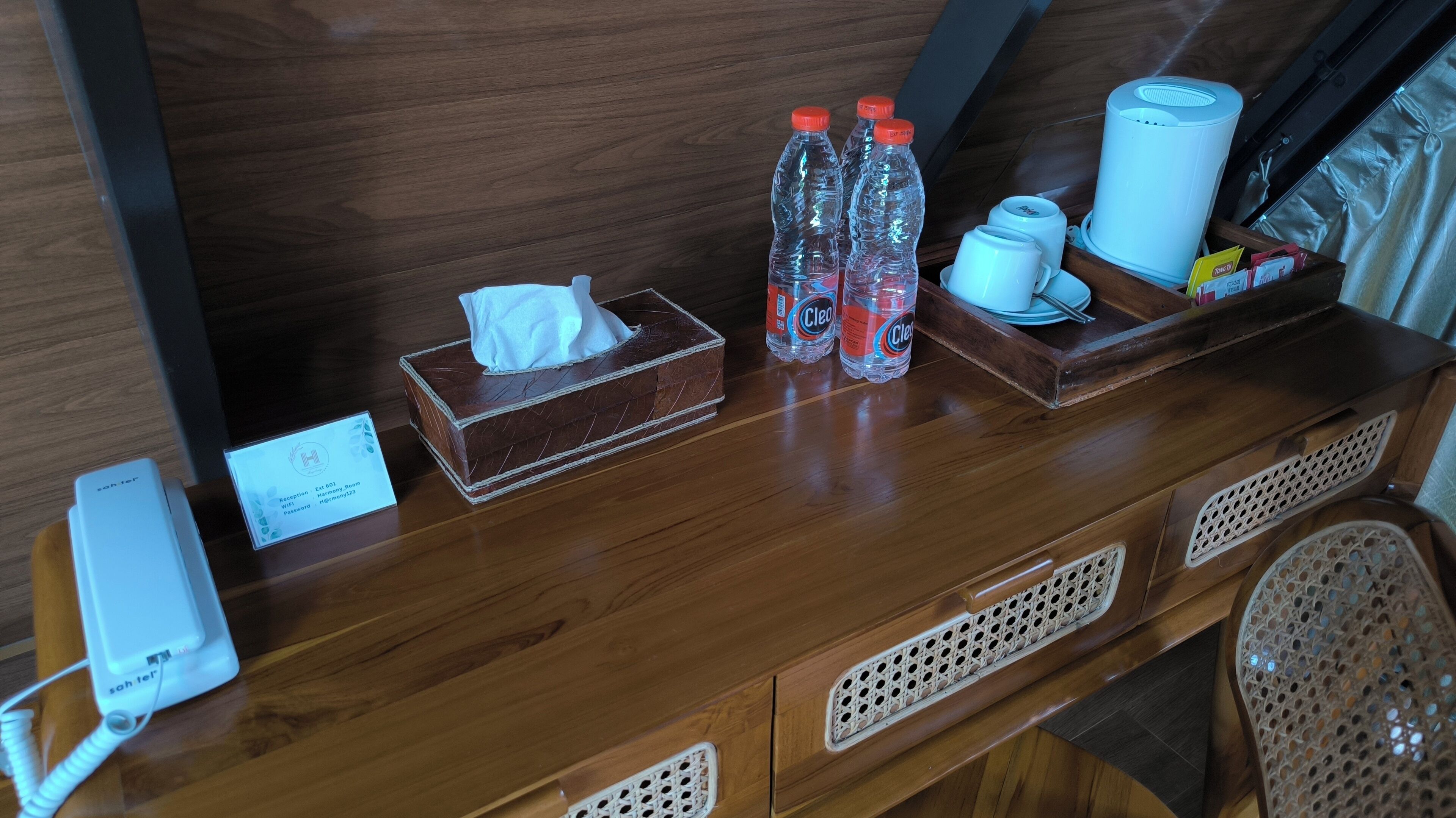 A wooden desk with a tissue box, two bottles of water, a coffee maker, and a phone.