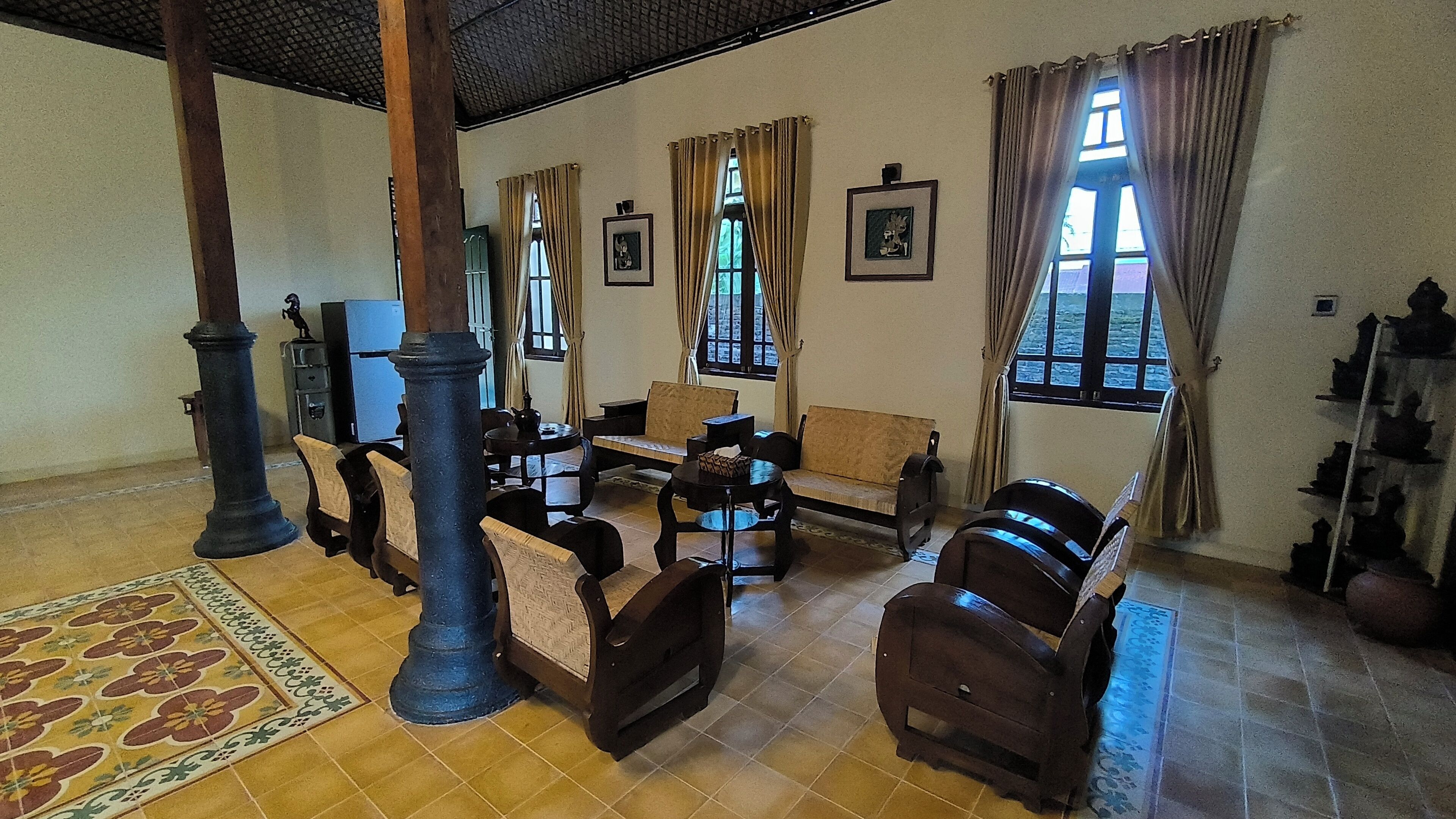 A traditional room with wooden furniture, a tiled floor, and large windows with curtains.