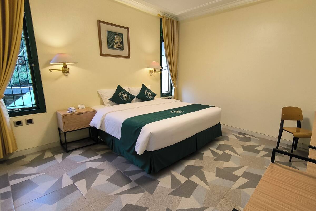Ein Hotelzimmer mit einem Bett, Nachttischlampen, einem Schreibtisch mit Stuhl, einem Spiegel und einem gemusterten Boden.