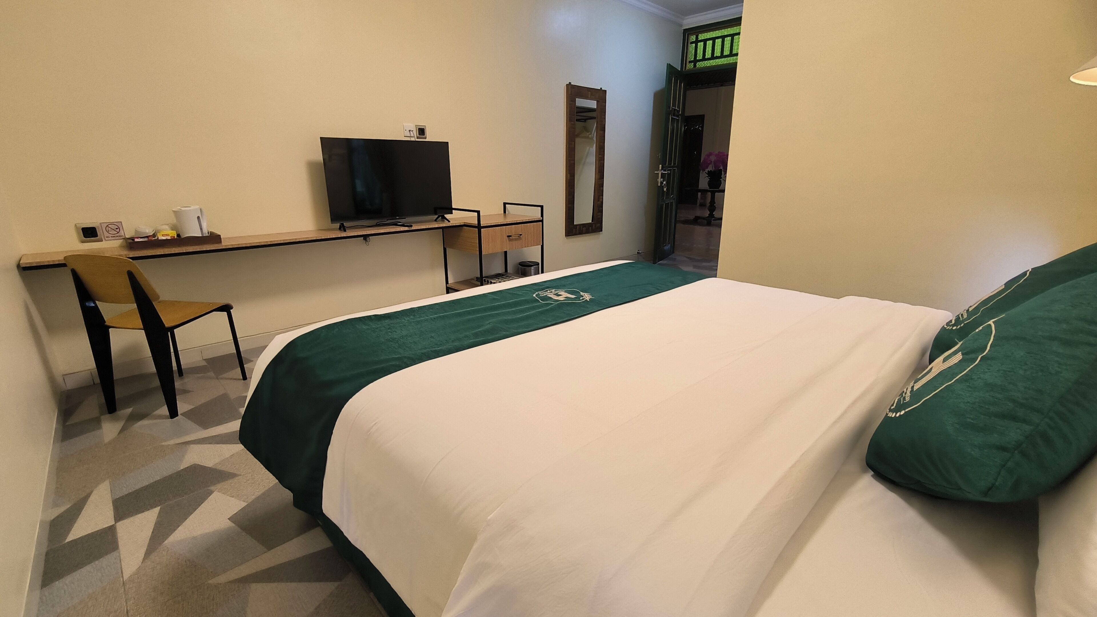 A hotel room with a bed, a desk, a chair, a television, and a mirror.