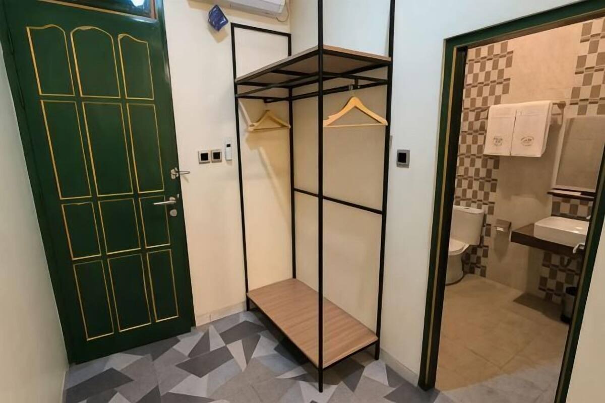 Ein Zimmer mit einer grünen Tür, einem Metallschrank, einem Badezimmer mit gefliesten Wänden und einem gefliesten Boden.