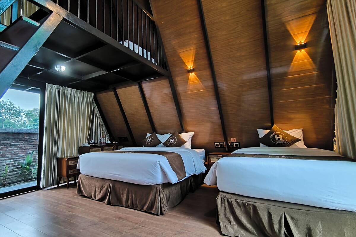 Ein modernes Hotelzimmer mit zwei Betten, Holzbalkendecke und einem großen Fenster mit Blick auf einen Garten.