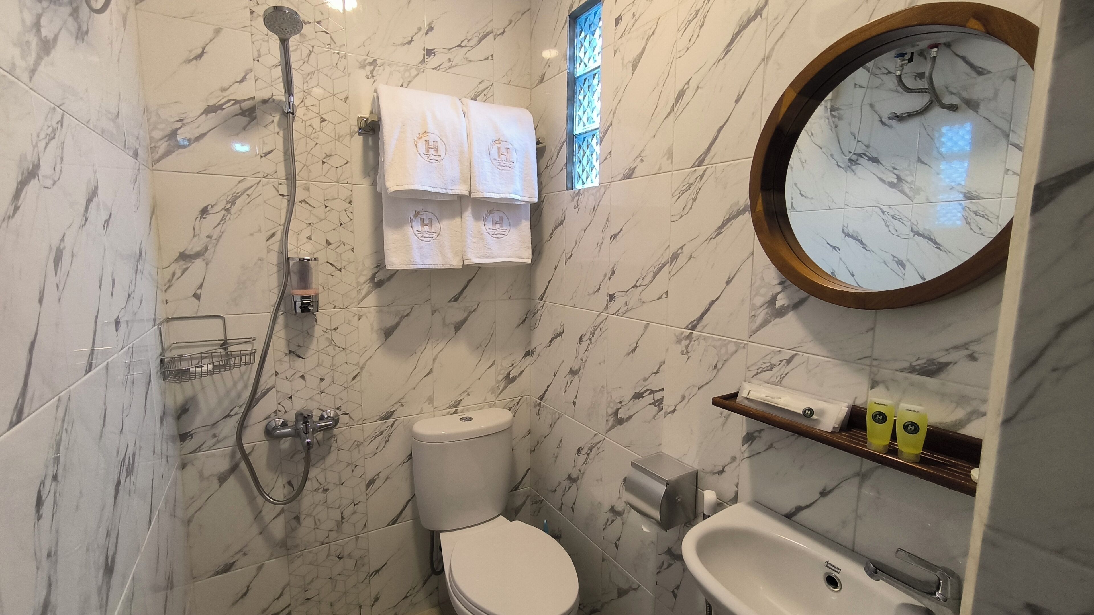 A bathroom with a toilet, sink, and shower. There are towels hanging on the wall and a mirror above the sink.