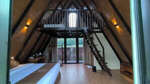 Une chambre mansardée avec un plafond haut, un plancher en bois, un lit, un bureau avec une chaise et un escalier menant à un niveau supérieur.