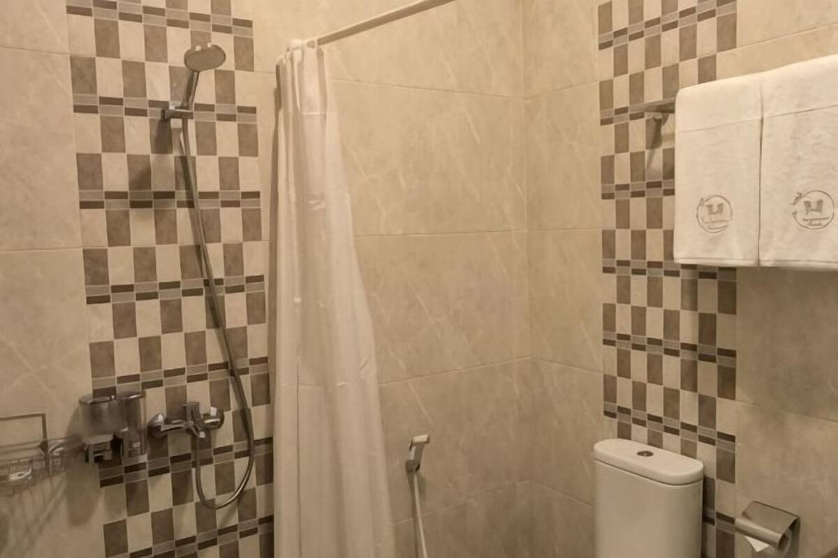 Une douche dont le carrelage présente un motif à carreaux, un porte-savon en verre et un porte-serviettes avec des serviettes.