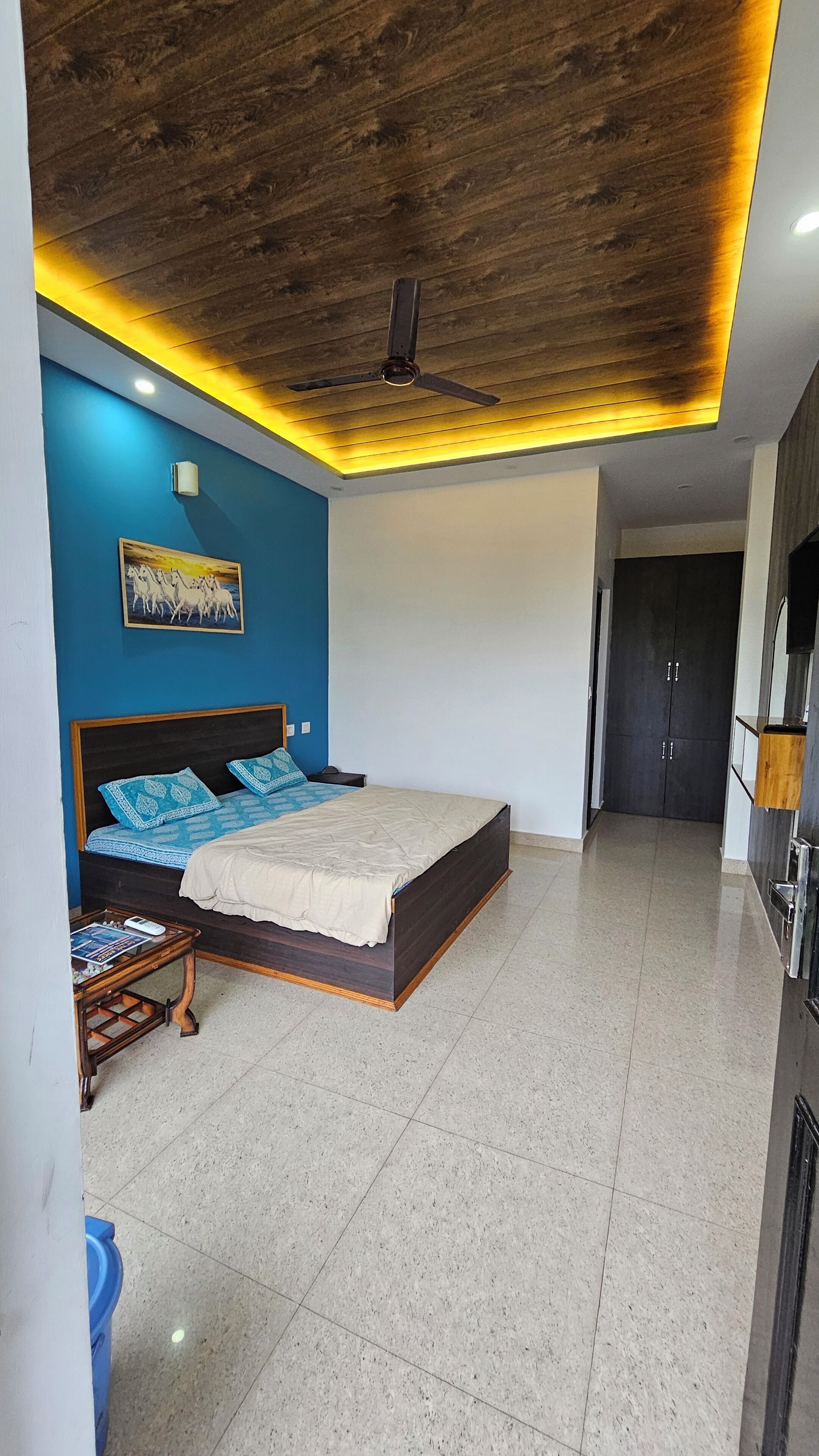 A bedroom with a bed, a ceiling fan, a nightstand, and a wall-mounted light.
