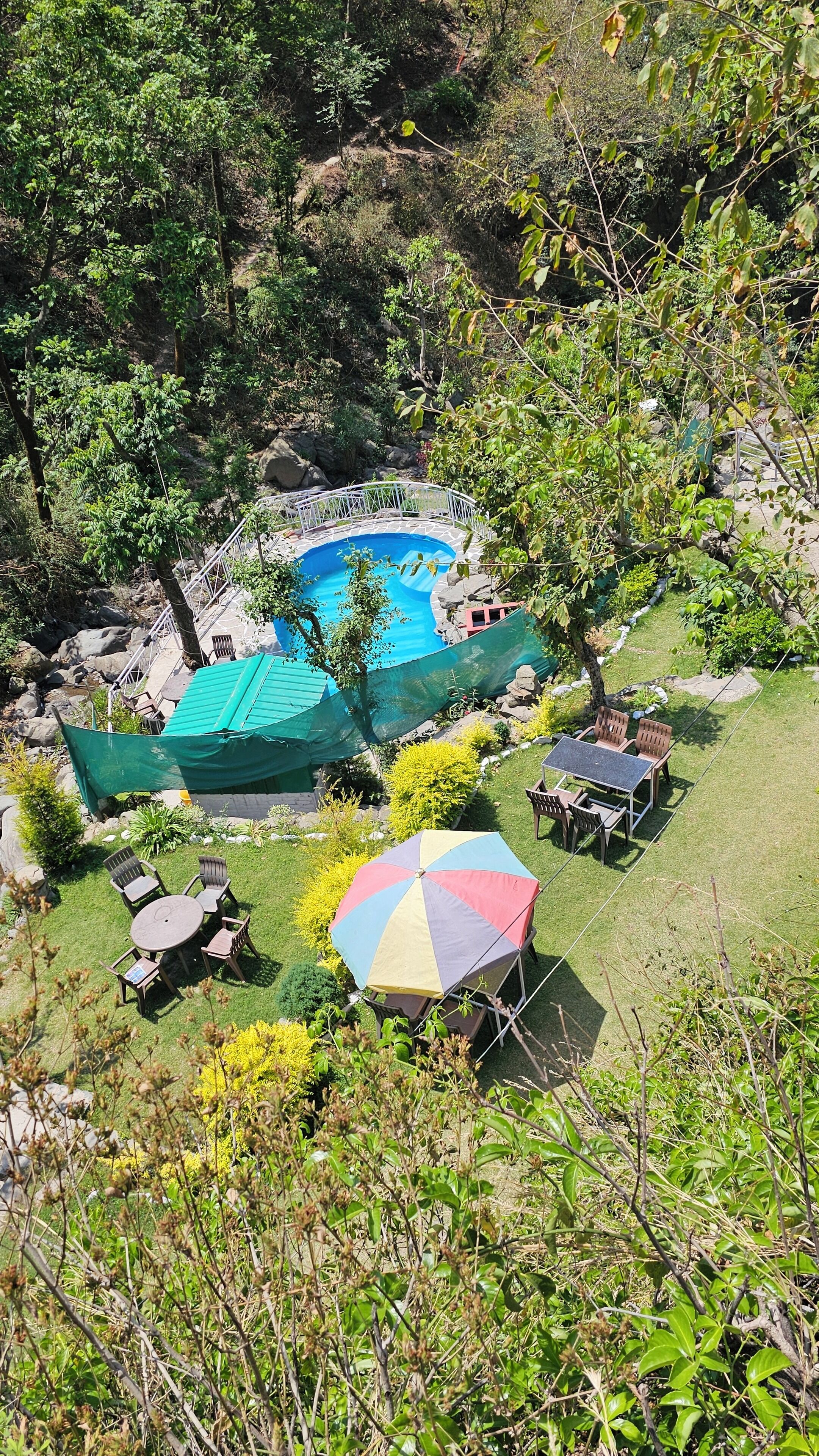 Une piscine entourée d’un jardin agrémenté d’une table et de chaises, ainsi que d’un parasol aux couleurs vives.
