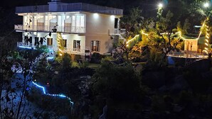 Une maison moderne à deux étages, dotée d’un balcon et entourée d’un jardin aménagé avec un élément décoratif aquatique.