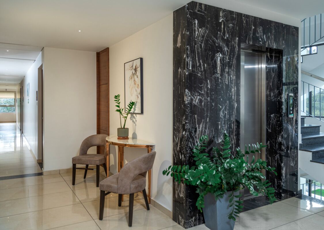 Een moderne lobby met een marmeren wand, een zithoek met twee stoelen, een tafel en een potplant.