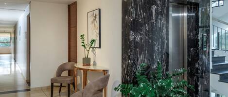Een moderne lobby met een marmeren wand, een zithoek met twee stoelen, een tafel en een potplant.