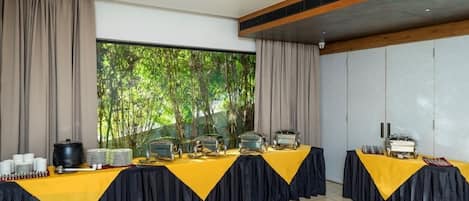 A conference room with a long table set for a buffet, large windows with a view of greenery, and a modern ceiling design.