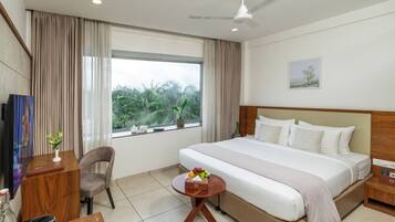 A hotel room with a large bed, a desk with a chair, a small table with a vase, and a window with curtains.