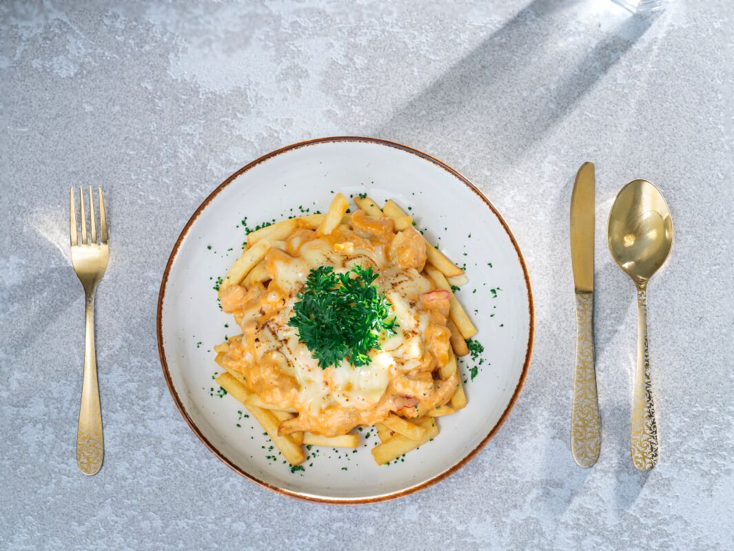 Un plato de pasta con decoración, acompañado por un tenedor y una cuchara sobre una superficie texturizada.