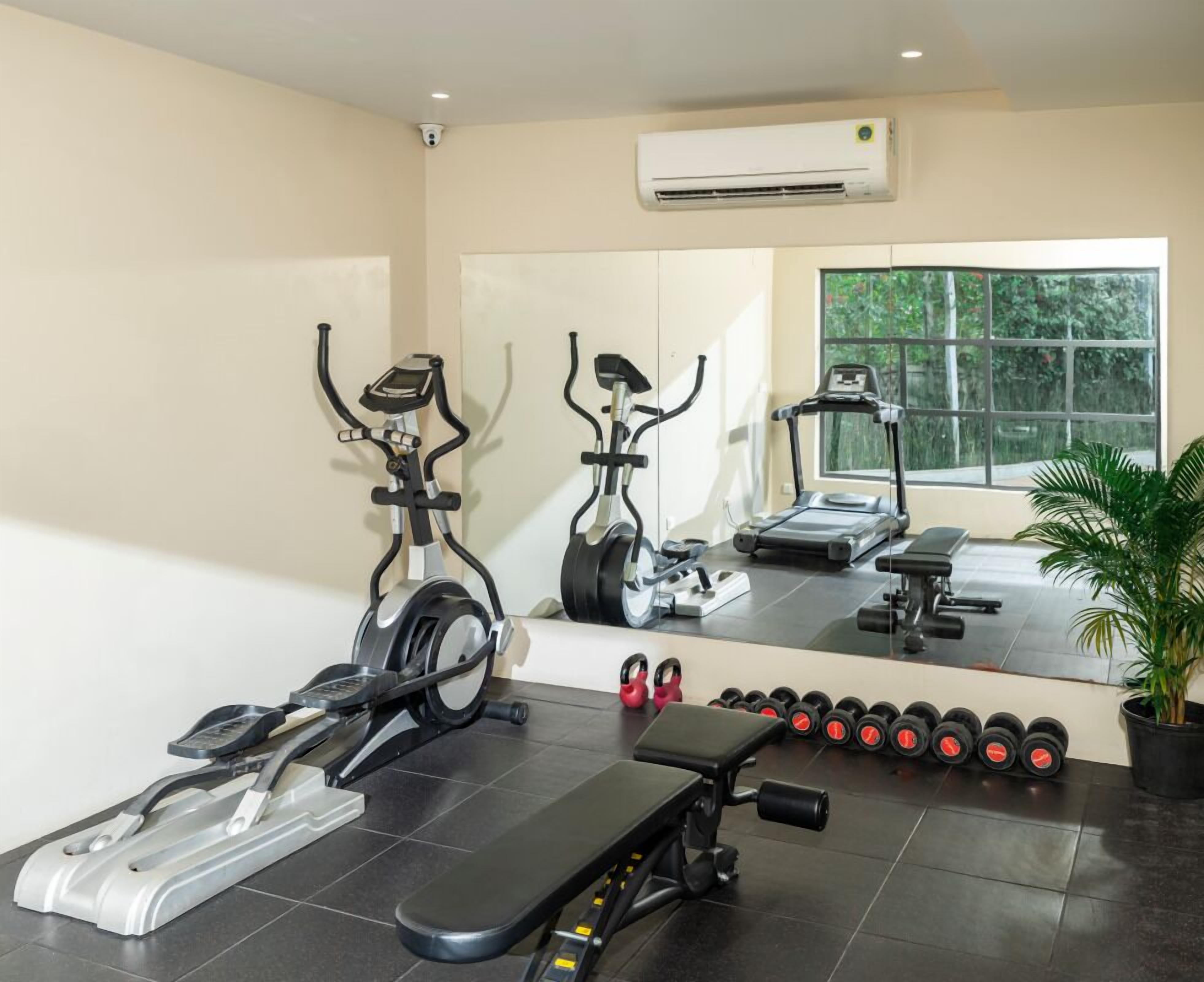 A gym with exercise equipment including treadmills, elliptical machines, and a bench.