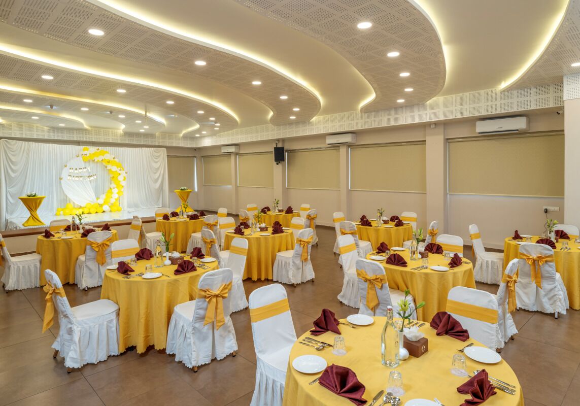 A banquet hall with round tables, white chairs, and yellow tablecloths.