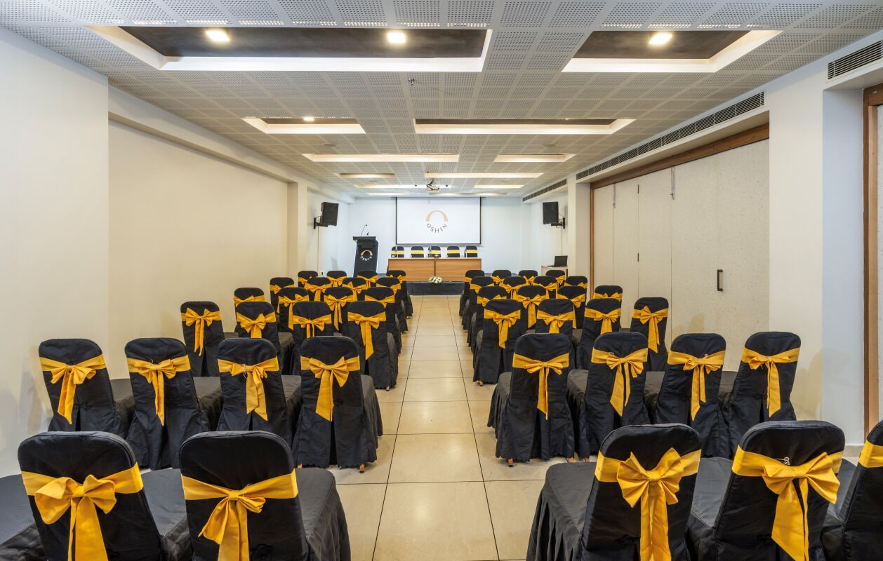 Un salón de conferencias con filas de sillas atadas con cintas amarillas, un atril y una pantalla al frente.