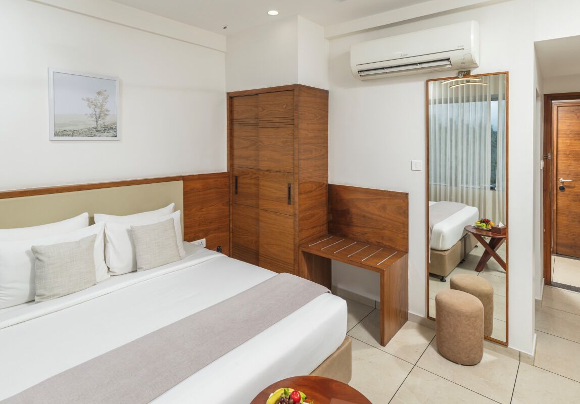 Habitación de hotel con cama, armario de madera, escritorio, aire acondicionado y baño con espejo e inodoro.