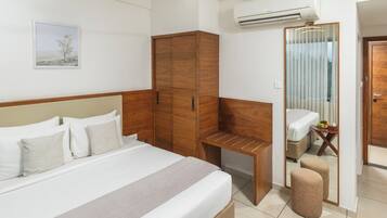 Habitación de hotel con cama, armario de madera, escritorio, aire acondicionado y baño con espejo e inodoro.