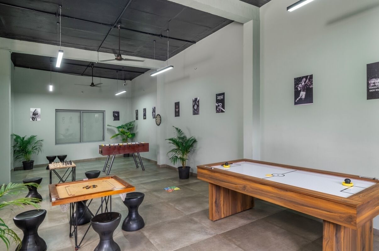 A room with a pool table, foosball table, and chess table. There are potted plants and a dartboard on the walls.