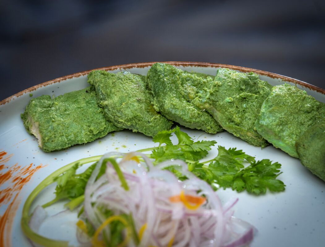 A plate with green food items and a side of sliced onions and cilantro.
