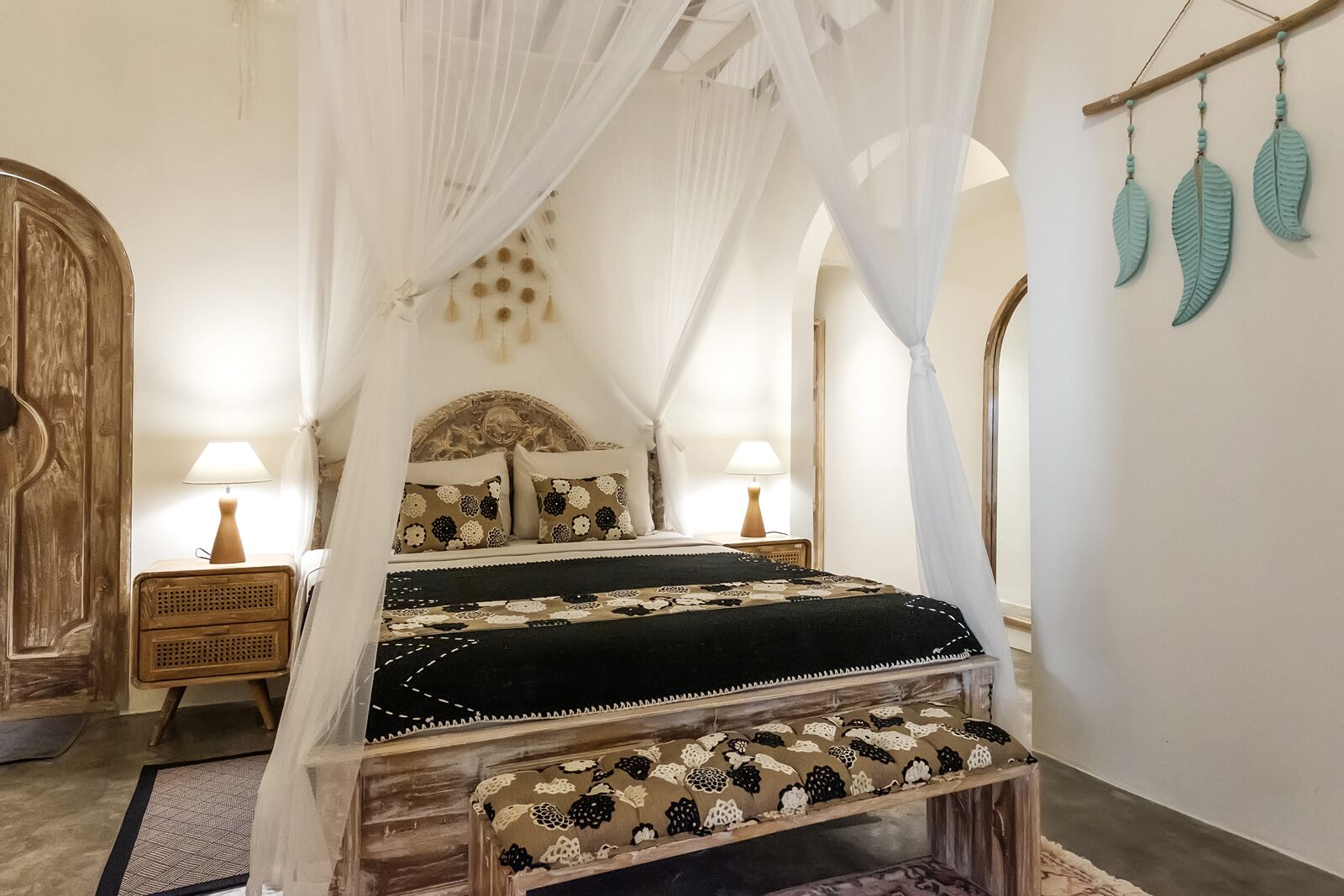 A bed with a canopy, two bedside tables, a bench, and decorative wall hangings.