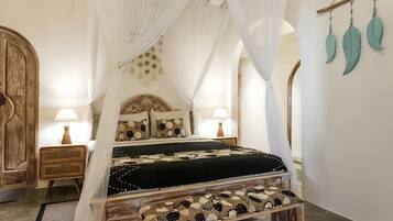 A bed with a canopy, two bedside tables, a bench, and decorative wall hangings.