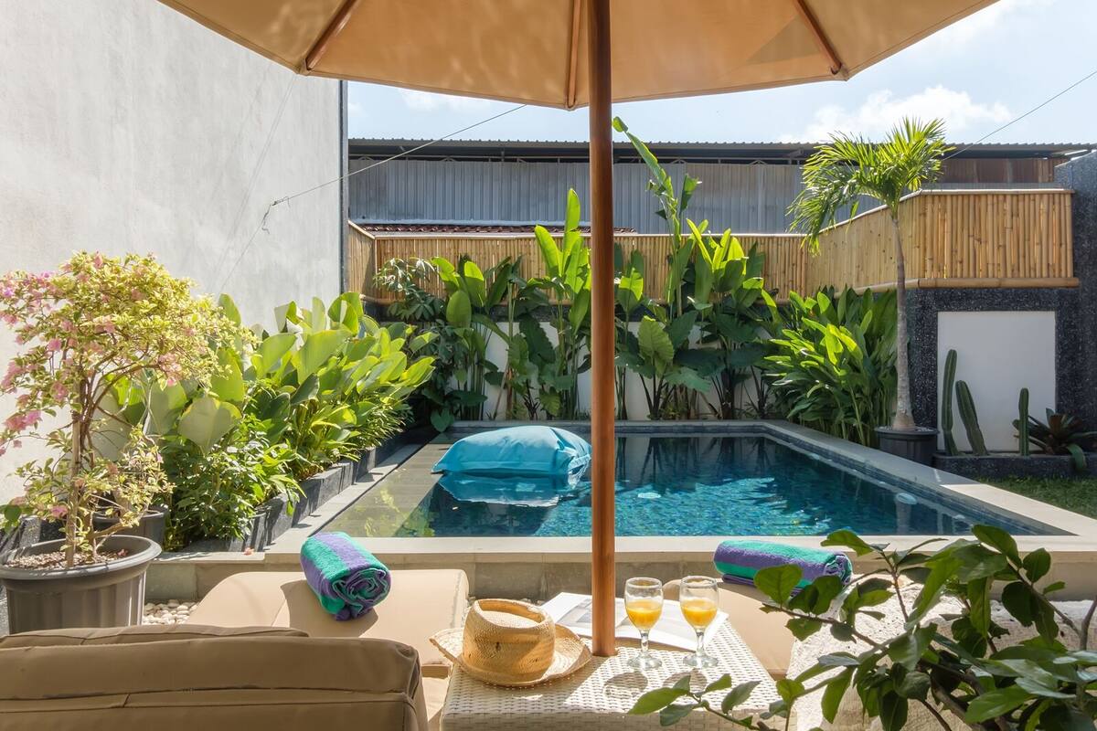 A pool area with a small pool, lounge chairs, and a table with drinks and a hat.