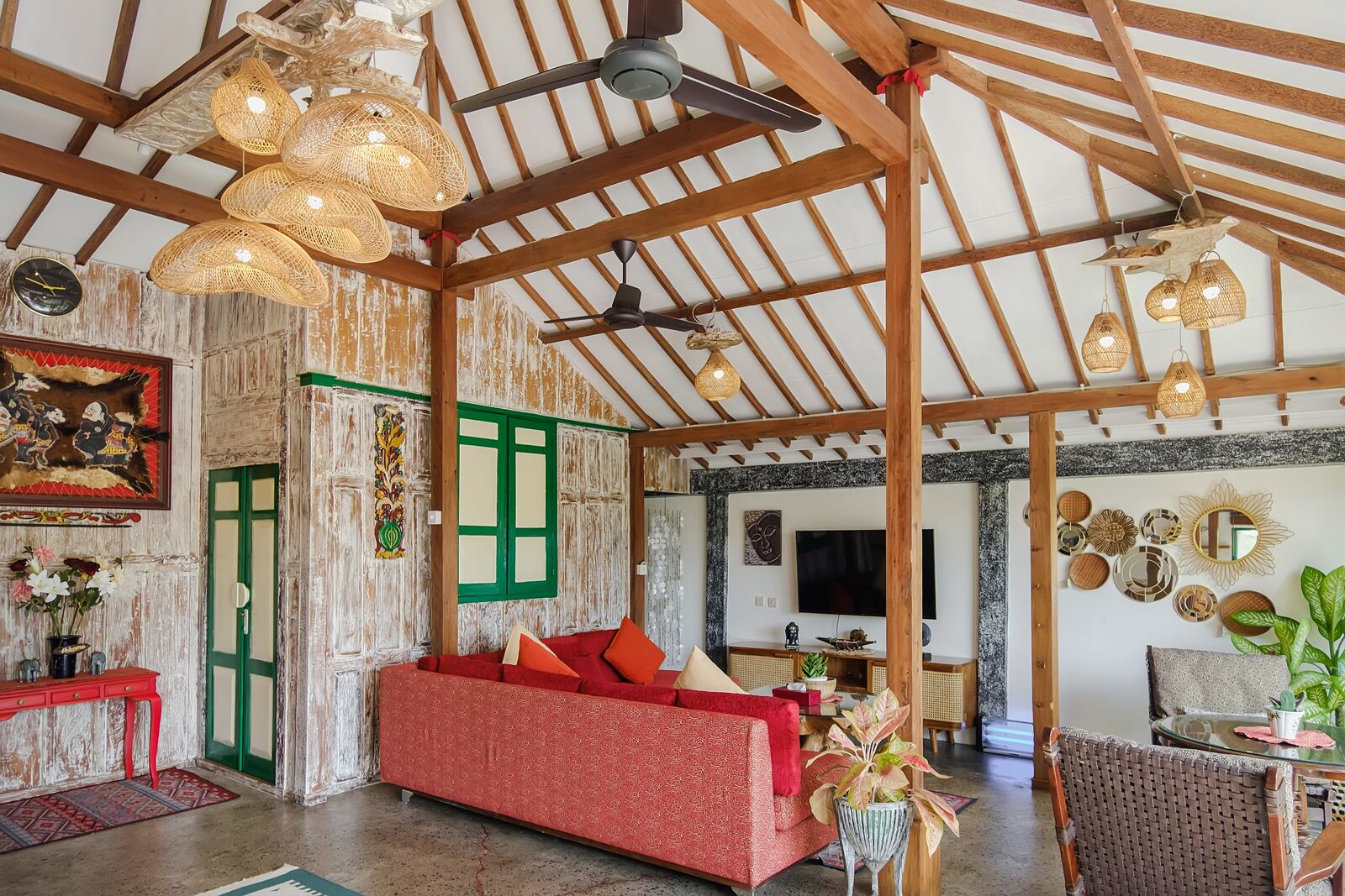 Un interior rústico con vigas de madera a la vista, un sofá rojo, lámparas de mimbre y decoración tradicional.